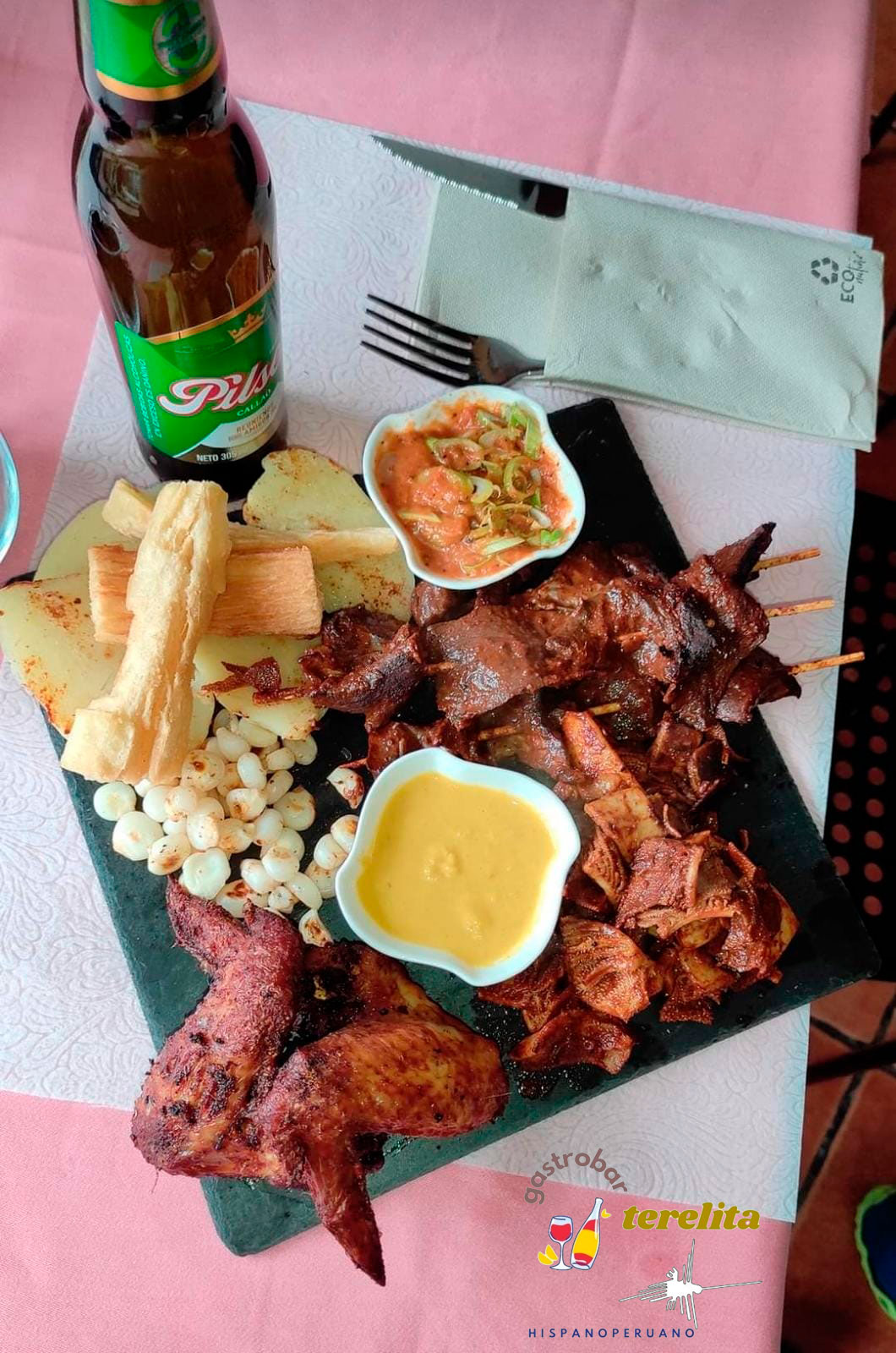 plato de pizarra con alitas de pollo, pinchos de carne y salsas con una cerveza